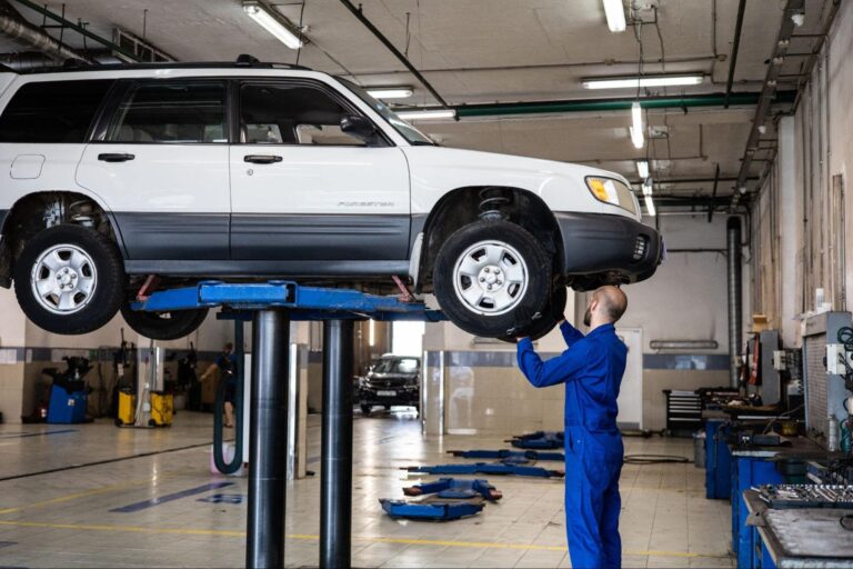 A the guy is inspecting a car in auto repair shop.